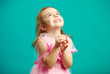 © Ilshat - Surprised little girl in beautiful pink dress clasped hands in front of her and looks up happily, isolated portrait on blue background.