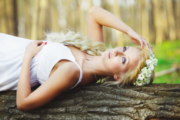 blond woman in white dress lying on tree in middle of the forest.