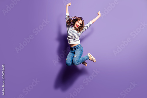 Fotografía Portrait of cheerful positive girl jumping in the air with raised fists looking at camera isolated on violet background