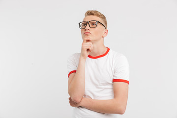 Poster - Image of thoughtful male student wearing eyeglasses looking upward while reflecting and touching chin, isolated over white background