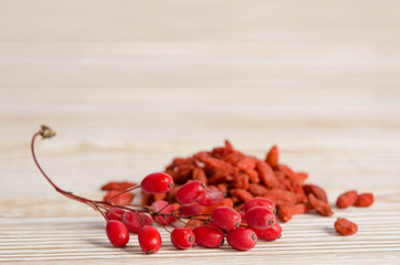 Wall Mural - Branch of ripe red barberries and dried goji berries on wooden table