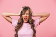 © Drobot Dean - Photo closeup of annoyed angry woman with long curly hair in basic t-shirt covering ears and screaming because of terrible noise, isolated over pink background