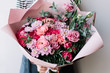 Very nice florist woman holding a beautiful blossoming flowers bouquet in pink colors of ranunculus, carnations, roses, pistachio leaves on the grey wall background