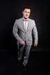 © AS Photo Family - Studio portrait of man in gray suit and bow tie against black background.