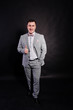 © AS Photo Family - Studio portrait of man in gray suit and bow tie showing thumb up against black background.