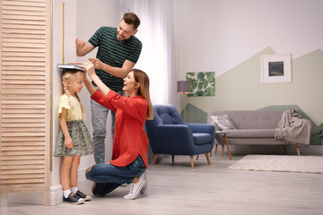 Parents measuring their daughter's height at home