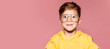 Little attractive boy in yellow jacket and big glasses. Funny child posing, pink wall on background. Close up portrait of smiling boy.