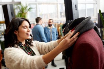 Wall Mural - sale, shopping, fashion and people concept - happy young woman choosing clothes at clothing store