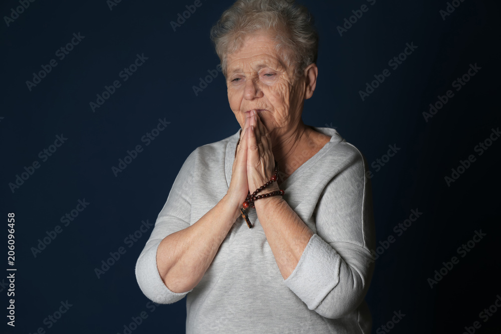 Religious elderly woman praying on dark background