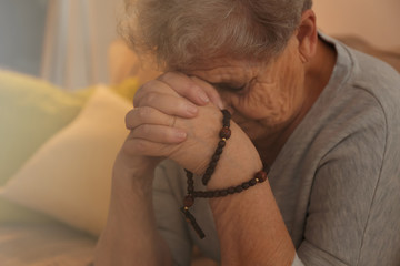 Wall Mural - Religious elderly woman praying with rosary beads, closeup