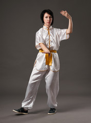 Young woman practicing tai chi chuan. Chinese management skill Qi's energy. Gray background, studio shoot.