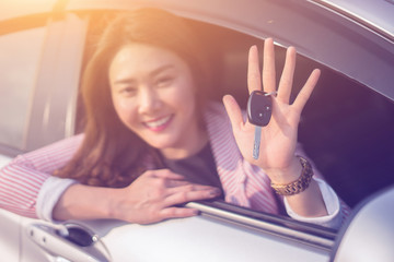 Asian driver woman smiling and showing new car key while sitting in a car that she taking it from dealer in the auto show. transport business, car sale for consumerism and people concept,vintage color