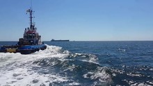 Tug Boat Making Waves As It Travels In The Black Sea During A Sunny Day Towards An Oil Tanker Ship