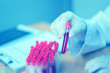 hand of a lab technician or medical doctor holding blood tube test and background a rack of color tubes  and microscope with blood samples other patients in laboratory