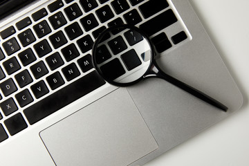 top view of magnifying glass and laptop on grey