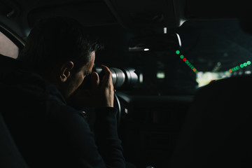 back view of focused man doing surveillance by camera with object glass from his car