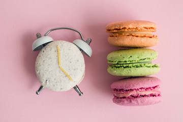 Wall Mural - Flat lay of colorful macarons on pastel pink background. One of them in shape of alarm clock.