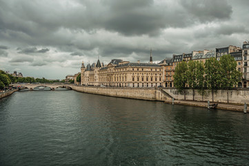 Wall Mural - Old buildings, promenade with lined trees on the bank of Seine River and cloudy sky in Paris. Known as the “City of Light”, is one of the most impressive world’s cultural center. Northern France.