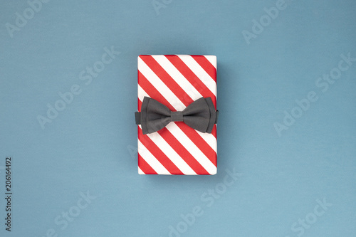 One gift box wrapped in red striped paper and tied with the grey bow tie on b...