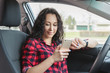 © Kot63 - Smiling brunette in car, looking at screen of  smartphone.