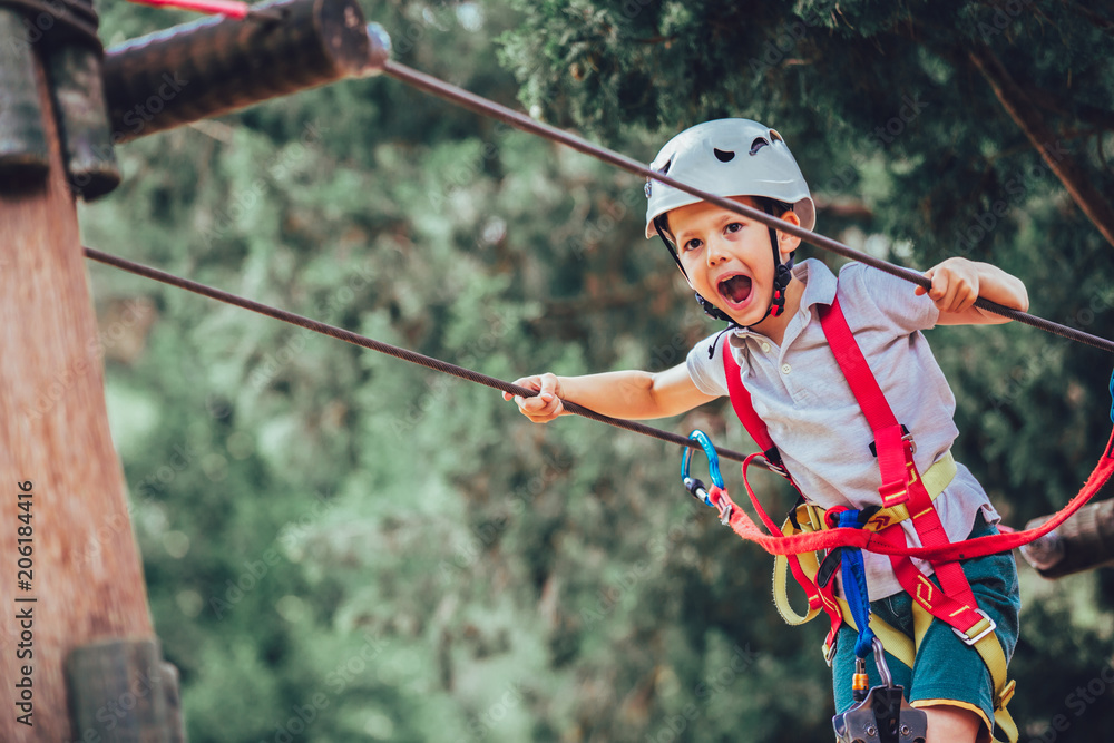 Little boy climbing in adventure activity park with helmet and safety equipment - obrazy, fototapety, plakaty 