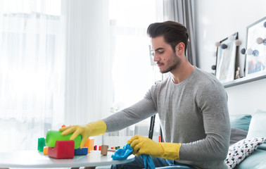 Young handsome father cleaning toys and table after playing with his child at home