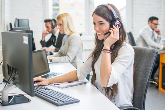 friendly smiling woman call center operator with headset using computer at office