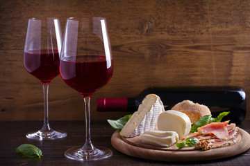 Glasses and bottle of wine with cheese, bread, nuts and jamon or prosciutto on dark wooden background. Wine and food concept