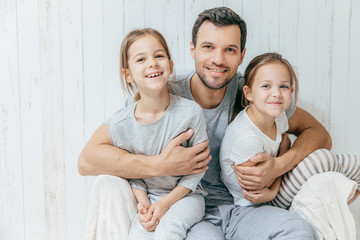 Father and kids. Paternity concept. Handsome unshaven affectionate dad embraces his two pretty dauhters, going to have walk together, have good relationship, pose at camera with positive smiles