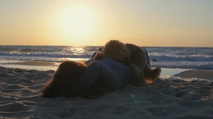 Wall Mural - Young woman with her dog lying and relaxing on the beach.