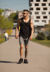 Wall Mural - View of young muscular man wearing black t-shirt and jeans walking on the streets of the modern city. Blurred background.