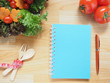 Blue spiral notebook for diet plan with pen, vegetables, spoon, fork and measuring tape on wooden table. Diet control or Healthy lifestyle concept. Copy space. Top view.
