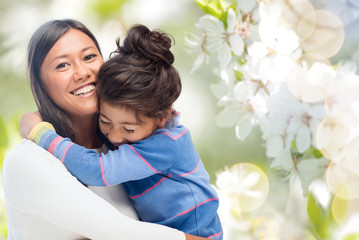 family, motherhood and people concept - happy mother and daughter hugging over cherry blossom backgr