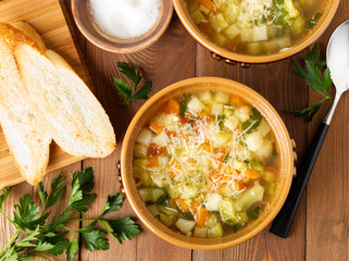 Two bowl of minestrone soup with toast on rustic wooden background, top view