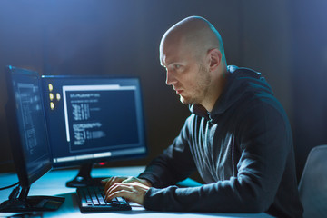 cybercrime, hacking and technology concept - male hacker in dark room writing code or using computer