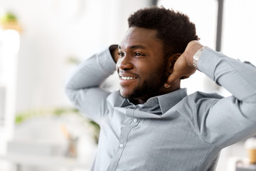 business and people concept - smiling african american businessman holding hands behind his head at office