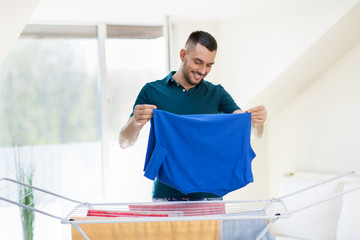 Wall Mural - laundry and household concept - happy man taking clothes from drying rack and putting them to basket at home