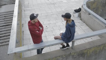 Poster - Top view of two people talking to each other. Beautiful young couple of man and woman standing on the edge of the building roof. City urban style. Slow motion video shooting by handheld gimbal