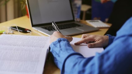 close up view of man left hand using pen for copy writing text from book desk top laptop computer monitor on background male student preparing exam study working writing notes wooden table copywriter