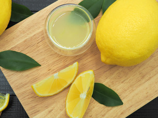 Fresh lemon juice in small bowl and lemon slice on dark wood background