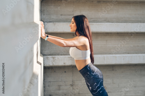 Sporty young woman doing standing wall push up triceps strength exercise during urban outdoor fitness workout.