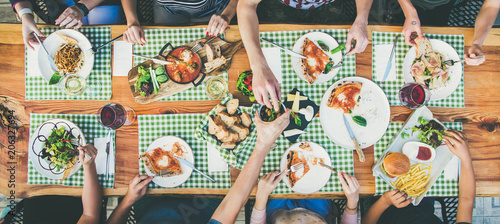 Family or friends summer party or outdoor dinner. Flat-lay of group of people at big table in cafe eating verious food together. Summer gathering or celebration concept © sonyakamoz
