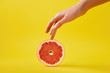 close up view of female hand and fresh grapefruit isolated on yellow