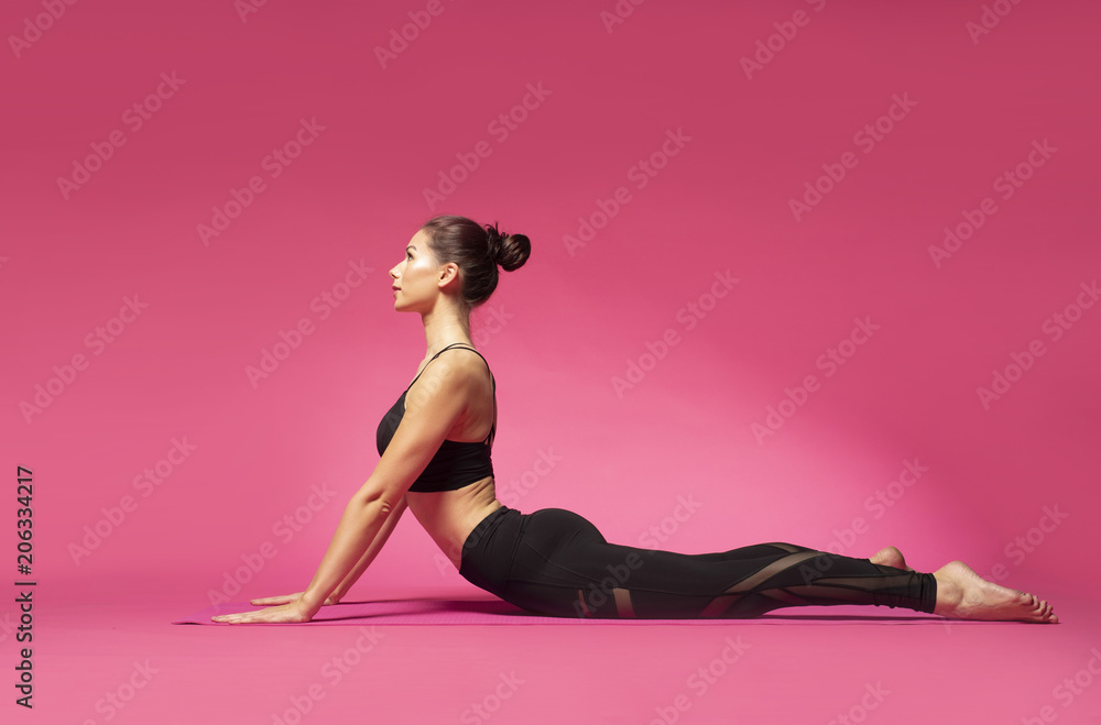 Long haired beautiful pilates or yoga athlete does a graceful pose while wearing a tight sports outfit against a pink background in a studio - obrazy, fototapety, plakaty 