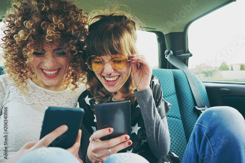 Fotografía Dos amigas usando sus teléfonos móviles mientras hacen un viaje en coche