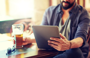 people, leisure and technology concept - close up of man with tablet pc computer drinking beer at bar or pub