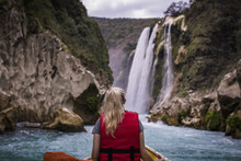 Rear View Of Woman Sitting In Boat On River Against Waterfall