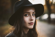 Close-up Portrait Of Woman Wearing Hat While Sitting At Park During Sunset
