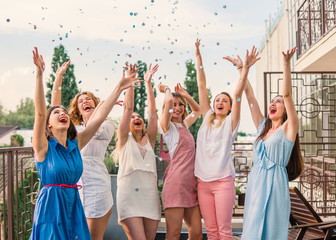 Girls Party. Beautiful Women Friends on the balcony Having Fun At Bachelorette Party. They are dancing in confetti with hands up