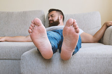 Close Up View Of Male Bare Feet. Bearded Adult Tired Sleeping Hipster Guy On Beige Sofa, Selective Focus